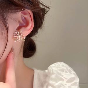 Détail de boucles d'oreilles flocon dorées avec perles et pierres de zircon brillantes