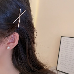 Close-up of sparkling diamond-set cross hairpin and pearl earring on a female model