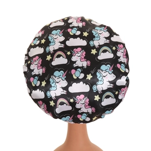 Macro detail of kids black satin bonnet featuring cute pink unicorn and rainbow patterns