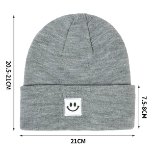 Gray knitted beanie with smiley face patch and detailed size measurements display