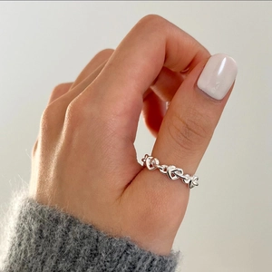 Macro detail of interlaced hollow heart silver ring worn on thumb with knitwear texture