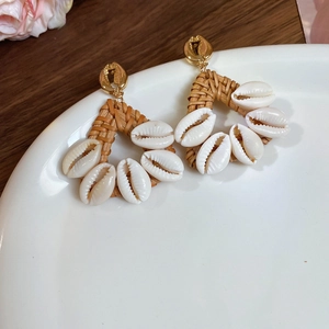 Macro view of woven rattan and white shell earrings on a white ceramic plate