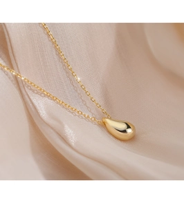 Close-up of golden teardrop pendant on fine chain over elegant beige silk background