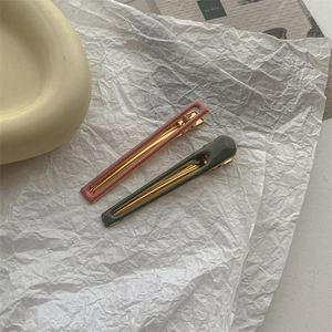 Close-up of pink and dark green hair clips with gold metal base on vintage paper
