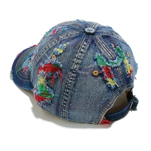 Dettaglio del cappellino in denim invecchiato con fori vintage e cuciture colorate a vista