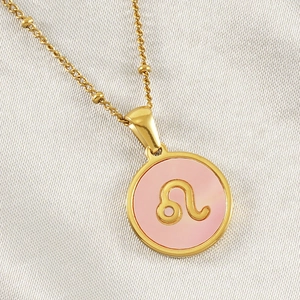 Detail of 18K gold titanium Leo constellation pendant with pink inlay on beige cloth