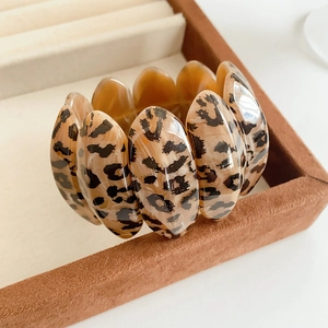 Detailed close-up of leopard print acrylic oval link bracelet on a brown suede jewelry box