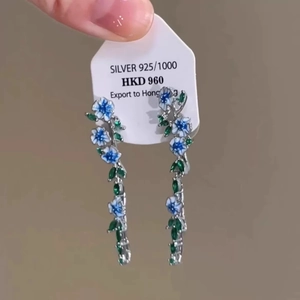 Detail of 925 silver earrings with blue flowers and green leaves on a white card tag