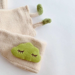 Close-up of beige knitted baby scarf featuring a green cloud with cute eyelash embroidery
