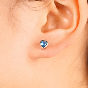 Close-up of blue heart-shaped gemstone stud earring with four-claw silver setting