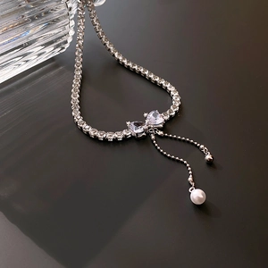 Close-up of zircon bow pendant with pearl tassels on a minimalist silver chain