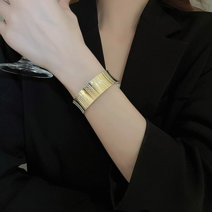 Detail of wide gold textured cuff bracelet showing vertical striped metal patterns