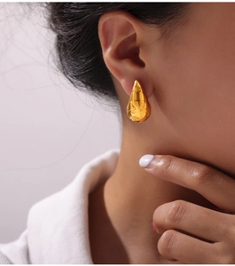 Macro shot of minimalist gold plated drop earrings showing polished texture on model