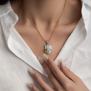 Elegant gold necklace with shield-shaped floral pendant and pearl flower on white shirt