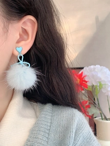 Close-up of light blue heart-shaped ear studs with delicate bow and fluffy pompom charms