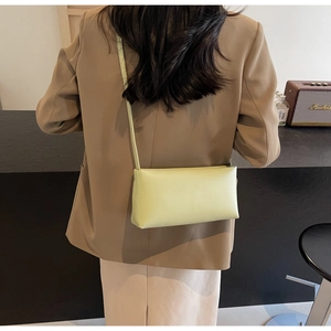 Rear view of a model wearing the light green faux leather shoulder bag in a warm interior