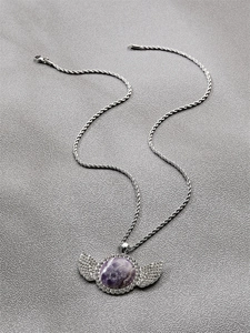 Vue détaillée du collier pendentif ailes d'ange en améthyste sur tissu texturé gris