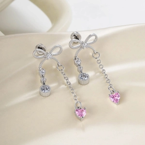 Silver bow earrings with pink heart and white zircon on beige silk background