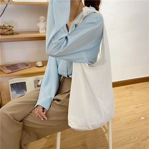 Lifestyle shot of white canvas tote bag worn on shoulder in minimalist interior decor