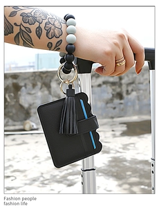 Detail of black leather card holder with tassel and silicone beaded wristlet on luggage