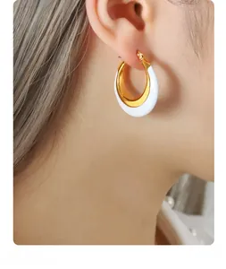 Close-up of golden hoop earrings with white enamel detail worn by a model