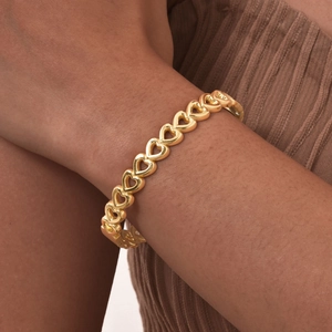 Detail of a hollow heart-shaped gold-plated stainless steel bracelet on a woman's wrist