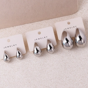 Three sizes of polished silver teardrop earrings displayed on a beige textured base
