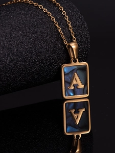 Macro view of a gold square necklace with dark blue shell and embossed letter A detail
