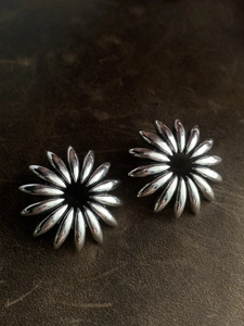 Macro detail of vintage silver sunflower earrings on dark leather textured background