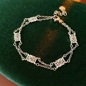 Macro detail of silver floral hollow bracelet on dark green velvet with heart charm