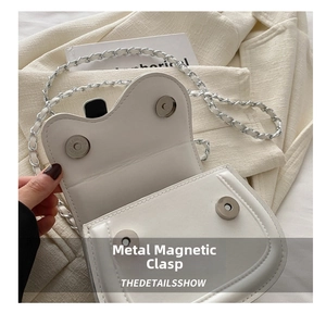Detail shot of the silver magnetic buckle closure and chain strap on a white bag