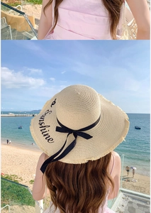 Detail of wide brim straw hat with black ribbon and a Sunshine embroidery on beach