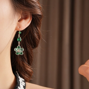 Detail of silver drop earrings with green zircon flowers worn by a model in soft light