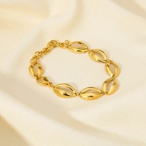 Detailed view of a gold shell-shaped chain bracelet resting on soft cream silk fabric