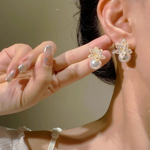 Detail of gold floral pearl earring with zircon petals worn on ear with soft lighting