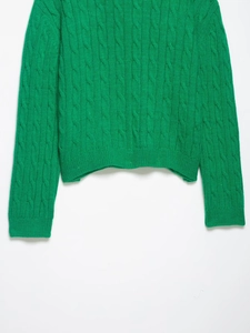 Detail of vibrant green cable knit sweater showing textured ribbed hem and cuffs
