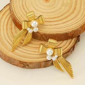 Elegant gold bow earrings with pearls and striped metal texture on natural wood backdrop