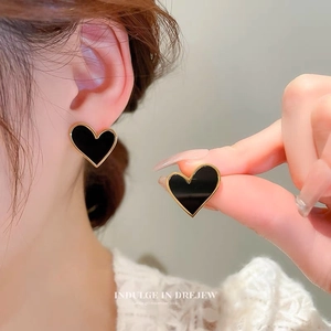 Elegant black heart stud earrings with gold trim worn by a model in a high-fashion style