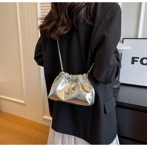 Close-up of silver pleated cloud bag featuring glossy finish and pearl charm accent
