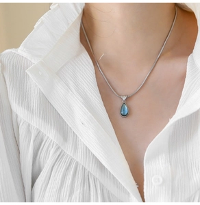 Detail of silver snake chain necklace with teardrop blue gemstone on model's neck