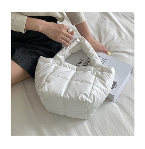 Top view of a white quilted puffer handbag on white bedding with minimalist styling