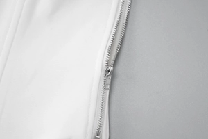 Detailed close-up of a silver metal zipper on the edge of a white fabric summer dress