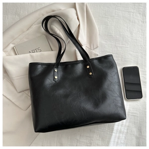 Detail of black faux leather tote bag showing smooth texture and golden rivet accents