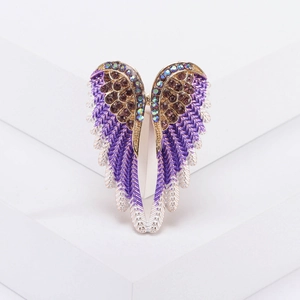 Golden angel wing brooch with purple rhinestones and enamel on a white stand
