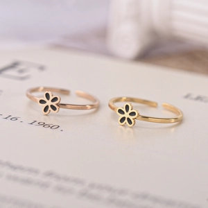 Macro detail of adjustable gold flower rings with black enamel petals on white surface