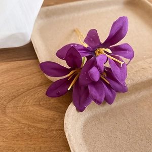 Macro shot of purple fabric flower hairpin with water droplets on petals and yellow core