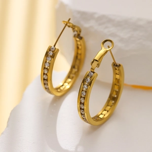 Macro detail of gold hoop earrings with sparkling cubic zirconia on textured stone