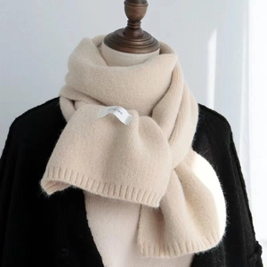 Detail of soft beige knitted scarf featuring a white brand label and warm texture