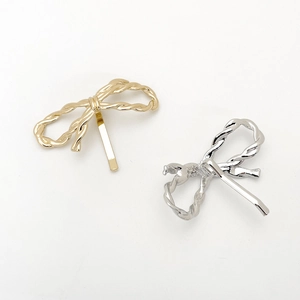 Detail of twisted metal bow hair clips in gold and silver finishes on white background