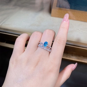 Detailed view of silver stackable rings set with blue oval stone on a finger